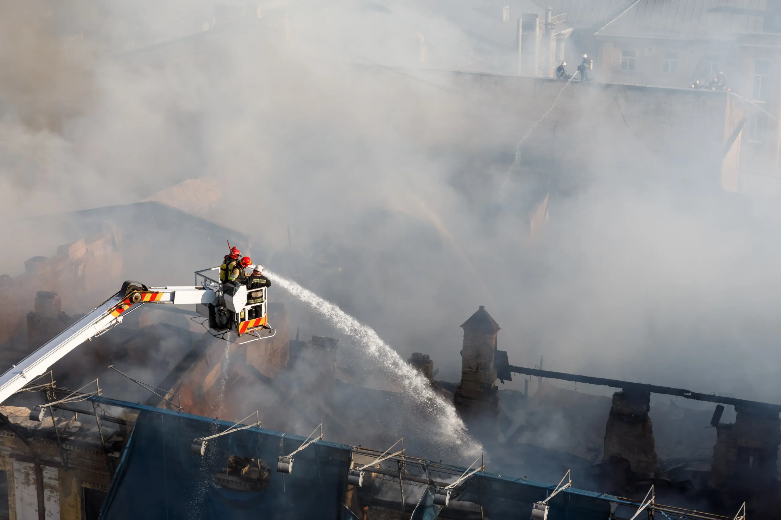 Firefighters on an aerial platform are extinguishing a large building fire amid heavy smoke